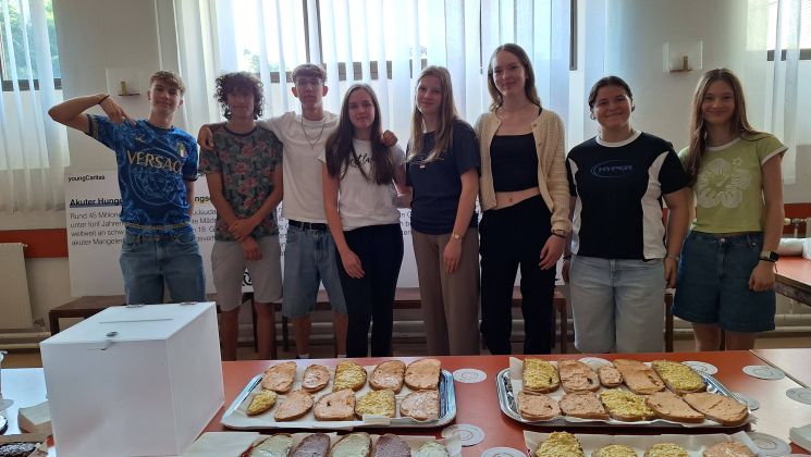 Gruppe von jungen Freiwilligen versammelt vor einer Tischreihe mit belegten Broten während einer eventuellen Wohltätigkeitsveranstaltung.
