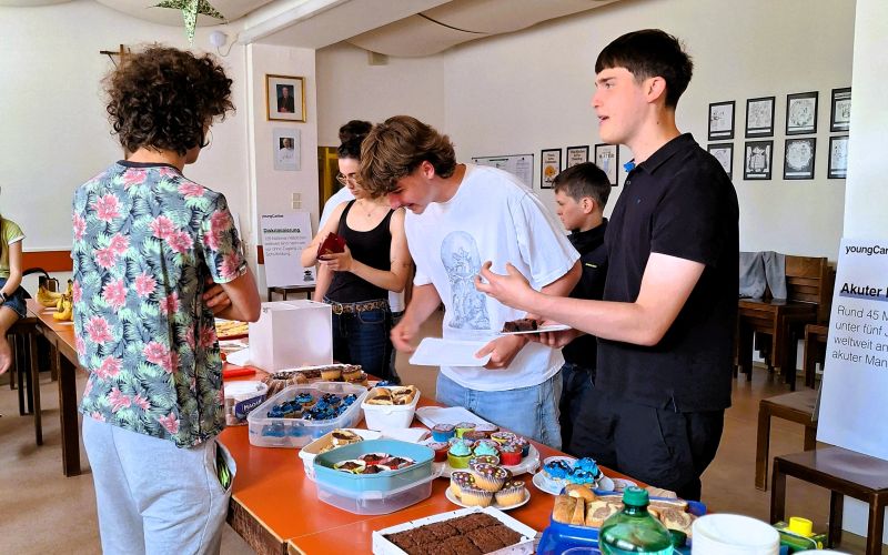 Mehrere Jugendliche stehen an einem Tisch mit Kuchen und bedienen sich.