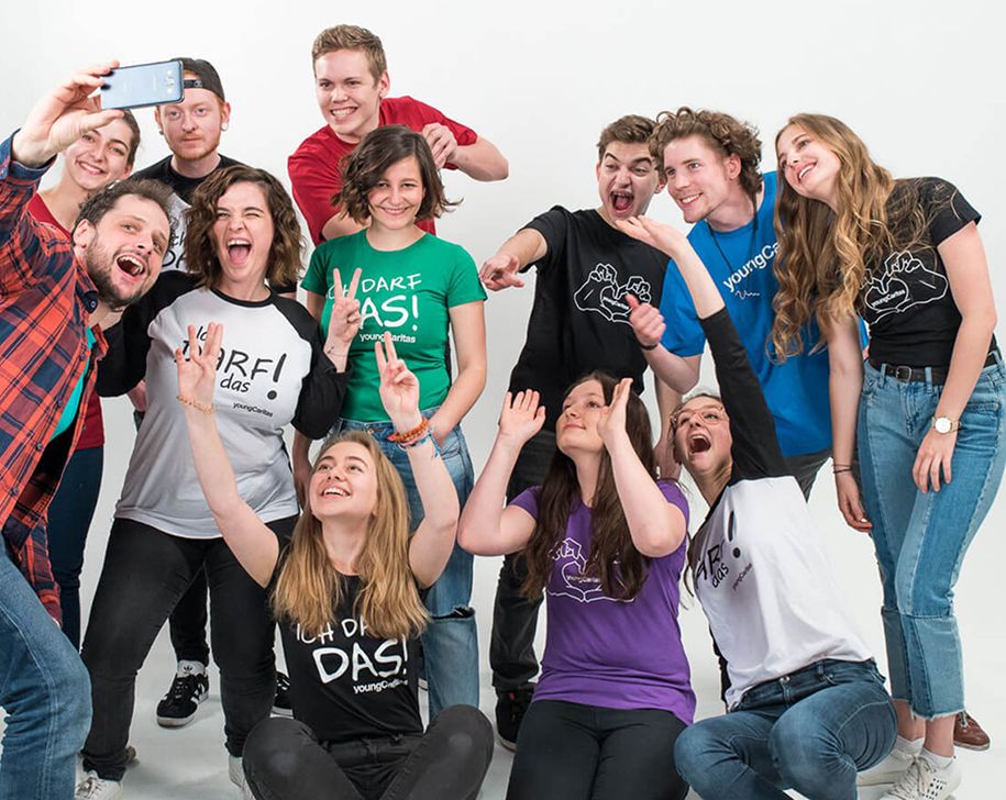 Gruppe junger Menschen, die fröhlich in die Kamera lächeln und hoch die Hände halten, während sie ein Selfie machen