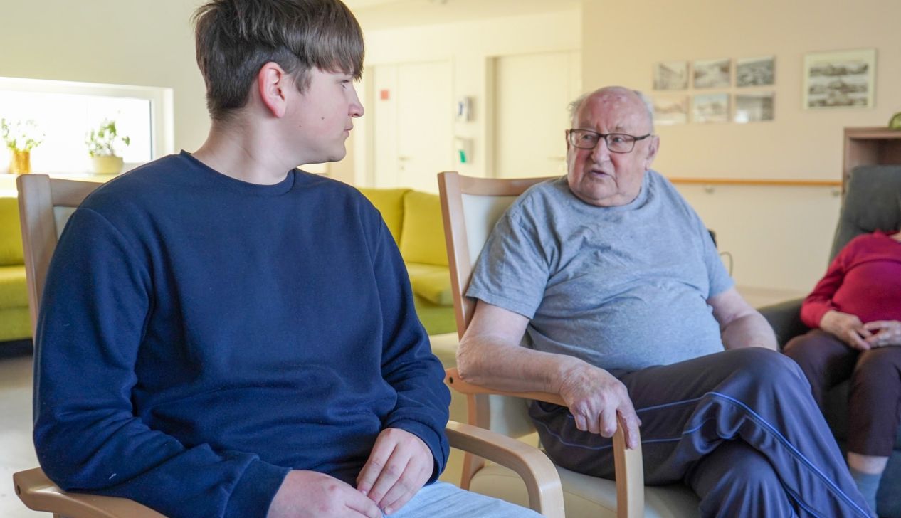 Ein junger Mann und ein älterer Herr sitzen sich nebeneinander und unterhalten sich.