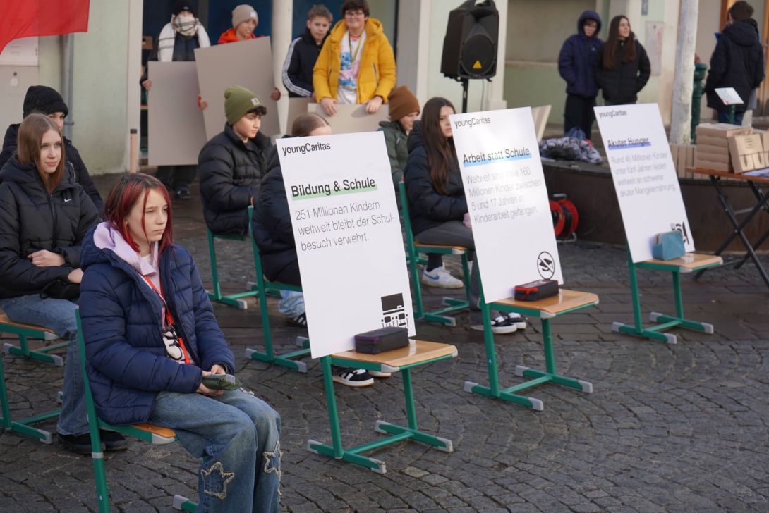 Schüler*innen sitzen auf Sesseln auf der Straße. Auf drei Sesseln stehen Plakate und liegen Federpenale.